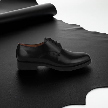 Black Blucher leather shoe displayed on a large black leather hide